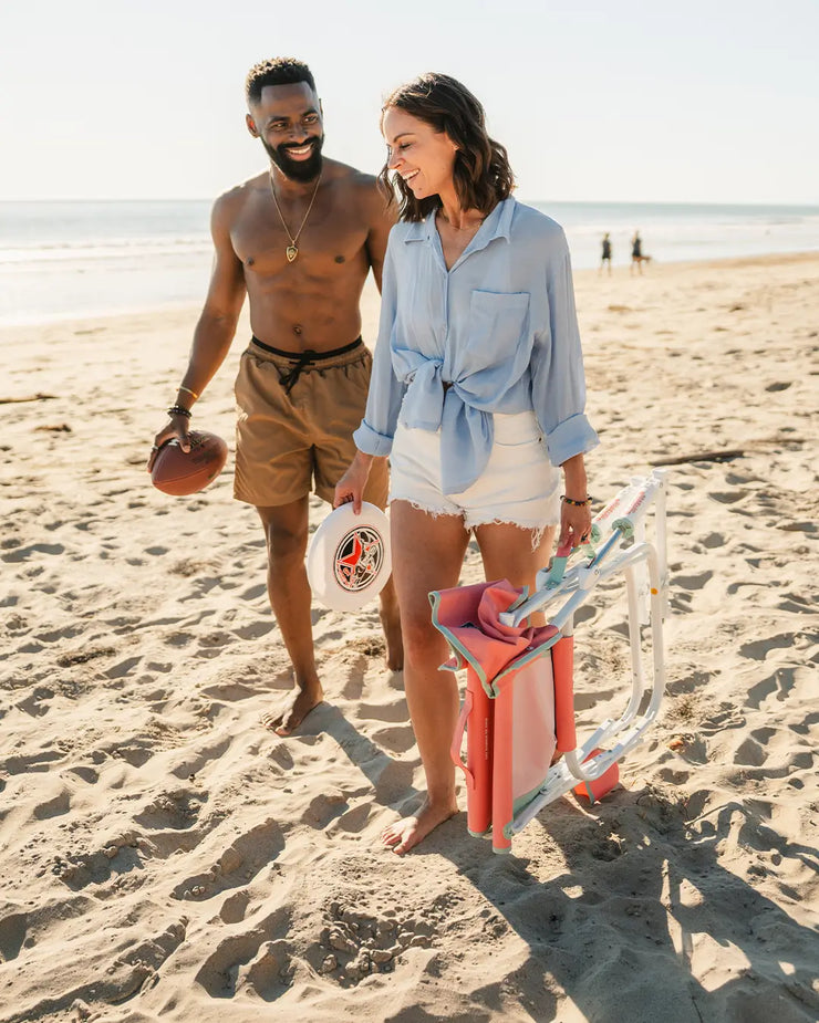 A couple walking together on a beach while a woman carries a pink Grab and Go Rocker.