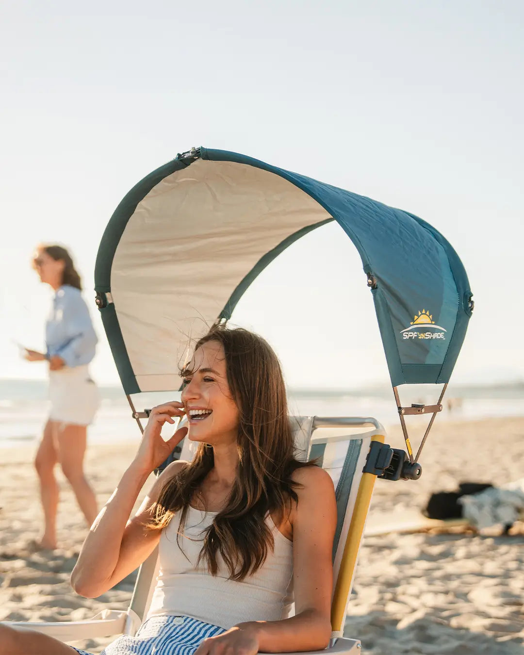 A woman sitting in a beach chair with an indigo Sunshade Accessory attached.